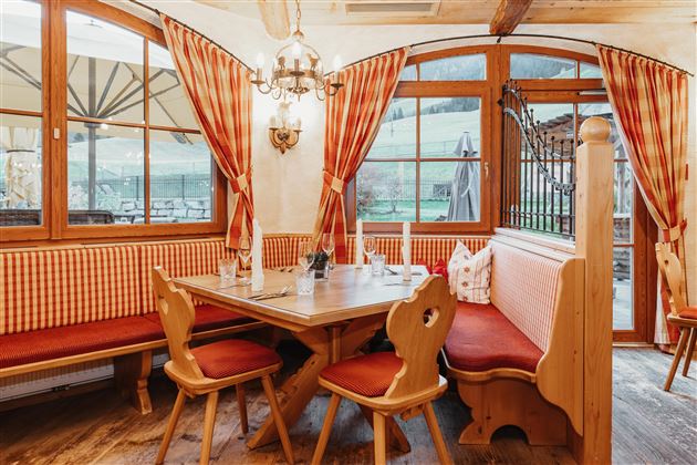 A cozy dining area with wooden furniture and red-and-white curtains. The table is set with plates and cutlery for the guests.