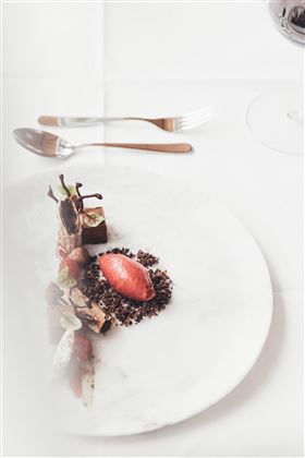An elegant dish presented on a white plate. The arrangement consists of various ingredients and a sorbet in the center.