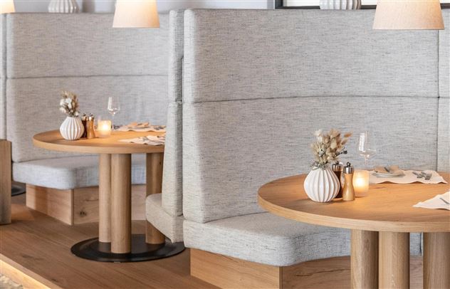 A modern restaurant with cozy benches and wooden tables. The subtle lighting creates an inviting atmosphere.