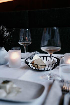 An elegantly set table with wine glasses and a bowl of bread. Soft candlelight creates a cozy atmosphere.