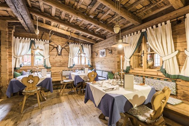A cozy restaurant with rustic wooden interior and traditional decoration. The tables are beautifully set and the windows let in a lot of light.