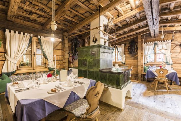 A cozy restaurant with wooden-paneled walls and traditional furniture. Elegant tablecloths and an elegant table decoration can be seen on the tables.