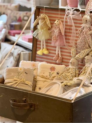 Eine dekorative Kiste mit Puppen und weichen Textilien. Die Puppen sind mit hübschen Outfits in Pastellfarben gestaltet.