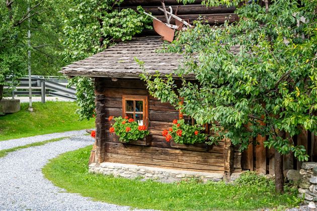 A charming wooden house with blooming windows.  
Surrounded by lush greenery and a winding path.