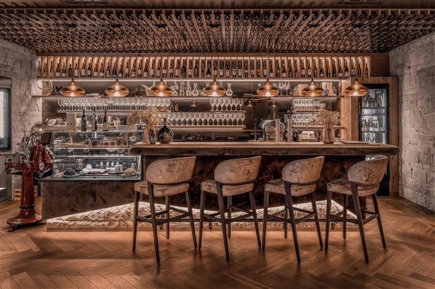 Eine stilvolle Bar mit Holzstühlen und einer eleganten Theke. Im Hintergrund sind Gläser und Flaschen ordentlich arrangiert.