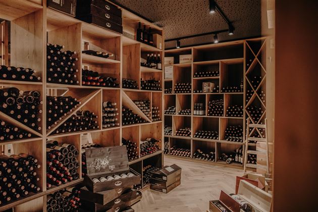 Ein Weinkeller mit vielen Regalen, gefüllt mit Weinflaschen. Die Holzregale sind ordentlich angeordnet und schaffen eine gemütliche Atmosphäre.