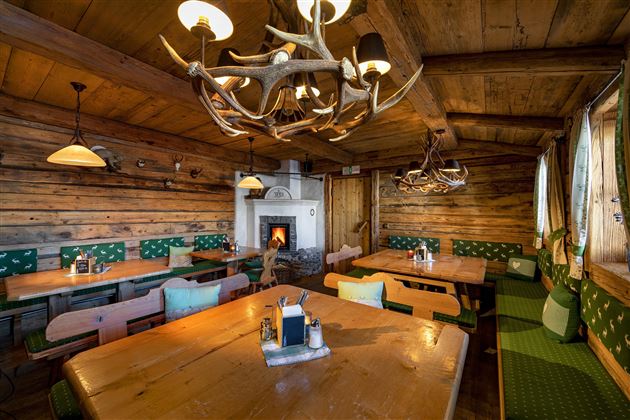 A cozy restaurant with wooden walls and a large fireplace. The tables are arranged simply and invitingly, with traditional furniture.