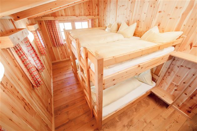 A cozy room with two wooden bunk beds. The walls are made of light wood, and there are large windows with checkered curtains.