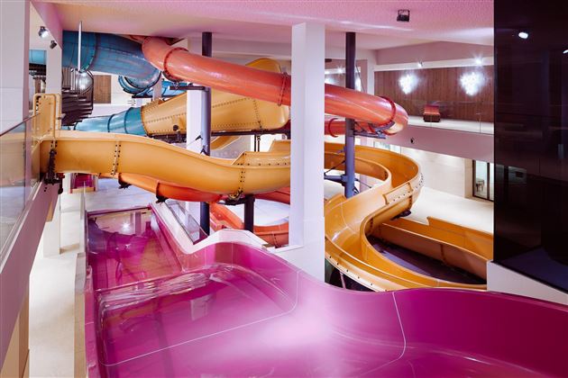 An indoor area with colorful water slides. The slides are in different colors and wind around a pool area.
