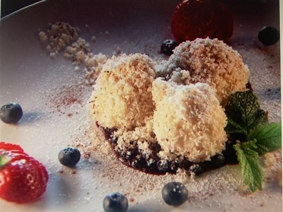 Eine köstliche Dessertpräsentation mit drei kugeligen Eiskugeln, bedeckt mit Kokosraspeln. Umrahmt von frischen Erdbeeren, Heidelbeeren und einer Minzeblatt-Dekoration.