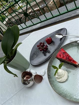 Ein eleganter Tisch mit einer köstlichen Torte und frischen Früchten. Neben einem Pflanztopf und einer Sonnenbrille zeigt es eine entspannte Atmosphäre.