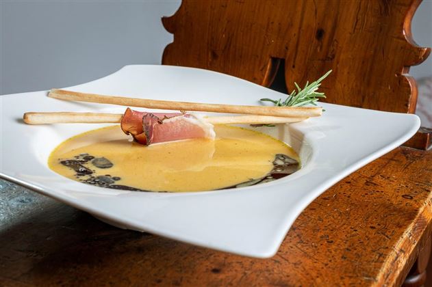 Eine kreative Suppe in einer eleganten Schüssel, garniert mit Schinken und Brotsticks. Im Hintergrund ist ein rustikaler Holztisch sichtbar.