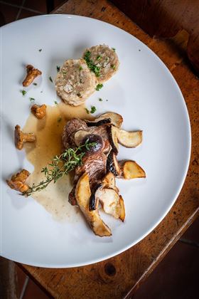 Ein Teller mit zartem Fleisch, gebratenen Pilzen und einer Beilage aus Semmelknödeln. Die Speise ist mit frischen Kräutern garniert und in einer delikaten Sauce angerichtet.