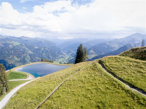 Eine malerische Berglandschaft mit einem klaren See. Saftige Wiesen und hohe Berge umgeben die Szene.