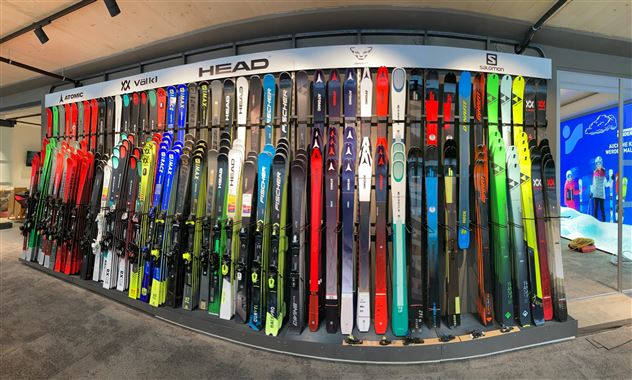 Eine Wand mit vielen verschiedenen Skiern in verschiedenen Farben und Designs. Die Skier sind ordentlich aufgereiht und präsentieren eine große Auswahl.