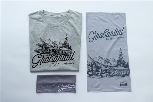 A gray T-shirt and a gray headband with the print "Grosartal - Valley of the Alps". There is also a large cloth with a mountain landscape and the same lettering.