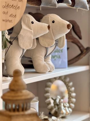 Zwei Stoffhunde stehen auf einem Regal. Im Hintergrund sind weitere Dekorationsobjekte sichtbar.