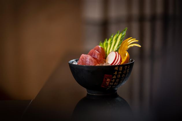 Eine Schüssel mit frischem Sashimi und buntem Gemüse. Der Teller ist geschmackvoll angerichtet und zeigt verschiedene Fischsorten mit einer attraktiven Garnitur.