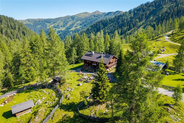 A picturesque mountain cabin surrounded by green forests and gentle hills. The landscape radiates tranquility and a connection to nature.