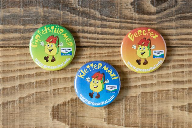Three colorful pins are lying on a wooden table. Each pin displays a cheerful face and a different inscription.