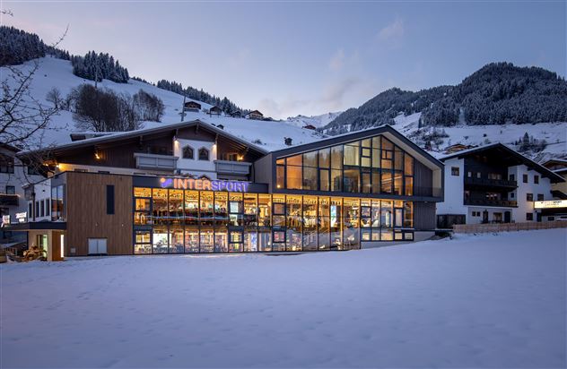 Ein modernes Gebäude mit großen Fenstern und einem geschäftigen Geschäft im Schnee. Im Hintergrund sind schneebedeckte Berge und eine ruhige Winterlandschaft zu sehen.