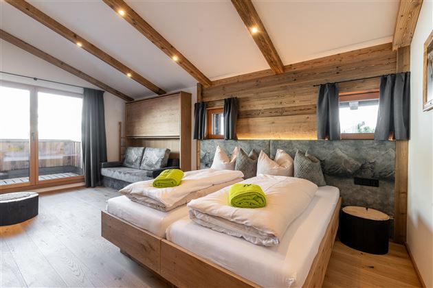 A modern hotel room with wooden ceilings and large windows. There are two beds with fresh towels and a cozy seating area.