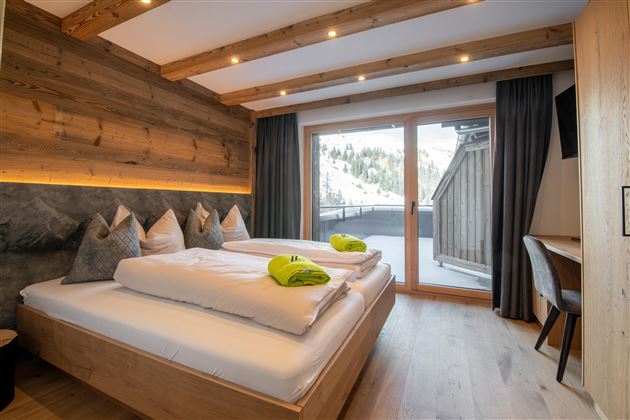 A modern hotel room with wooden furniture and a large window. The ambiance is cozy and bright, ideal for relaxation.