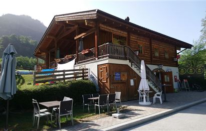 Ein charmantes Holzhaus in malerischer Umgebung. Tische und Stühle laden im Freien zum Verweilen ein.