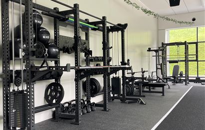 Ein moderner Fitnessraum mit verschiedenen Trainingsgeräten und Gewichten. Der Raum ist gut beleuchtet und hat einen klaren, funktionalen Stil.