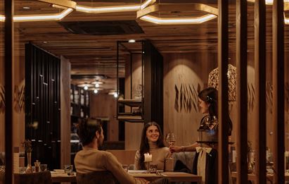 An elegant restaurant with warm lighting. Two guests enjoy their meal while a waitress serves at the table.