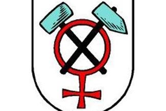 Ein Wappen mit einem roten Symbol, das eine Frau darstellt, umgeben von zwei blauen Werkzeugen. Es symbolisiert die Verbindung von Feminismus und Handwerk.