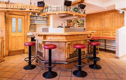 Eine gemütliche Bar mit Holzinterieur und roten Barhockern. Der Raum hat eine einladende Atmosphäre, ideal für gesellige Treffen.