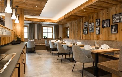 A modern restaurant with wooden paneling and elegant chairs. The tables are set, and decorative pictures hang on the wall.