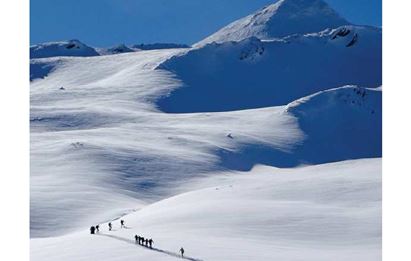 Eine winterliche Landschaft mit schneebedeckten Bergen und einer Gruppe von Skitourengehern. Der Himmel ist klar und blau, ideal für Outdoor-Aktivitäten.