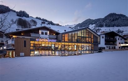 Ein modernes Gebäude mit großen Fenstern und einem geschäftigen Geschäft im Schnee. Im Hintergrund sind schneebedeckte Berge und eine ruhige Winterlandschaft zu sehen.