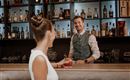 Ein freundlicher Barkeeper steht hinter der Bar und serviert einen Cocktail. Die Atmosphäre ist elegant und einladend.