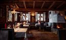 Ein gemütliches Restaurant mit Holzelementen und einer warmen Atmosphäre. Tische sind mit stilvollem Geschirr und Dekoration gedeckt, und im Hintergrund brennt ein Kamin.