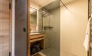 A modern bathroom with a glass shower and a wooden shelf. The decor is simple and elegant.