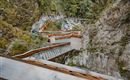 A wooden staircase winds through an impressive rock landscape. Below, a small stream flows between the stones.