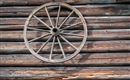 An old wooden wheel hangs on a rustic wooden wall. The structure of the wall emphasizes the vintage aesthetic.