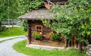 A charming wooden house with blooming windows.  
Surrounded by lush greenery and a winding path.