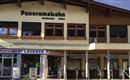 A building with a sign "Panoramabahn" and shops underneath. There are large windows and an inviting entrance area.