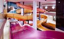 An indoor area with colorful water slides. The slides are in different colors and wind around a pool area.