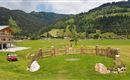 A picturesque landscape with green meadows and gentle hills. In the foreground, there is a wooden fence with some stones as well as a golf cart.