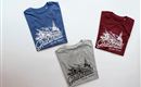 Three T-shirts in different colors are lying on a white background. Each shirt features a colorful design with a mountain motif and the inscription “Grasaital – Valley of the Pastures.”