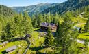 A picturesque mountain cabin surrounded by green forests and gentle hills. The landscape radiates tranquility and a connection to nature.