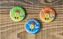 Three colorful pins are lying on a wooden table. Each pin displays a cheerful face and a different inscription.