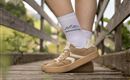 Comfortable sneakers are on a wooden walkway. In the background, green meadows and trees are visible.