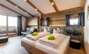 A modern hotel room with wooden ceilings and large windows. There are two beds with fresh towels and a cozy seating area.