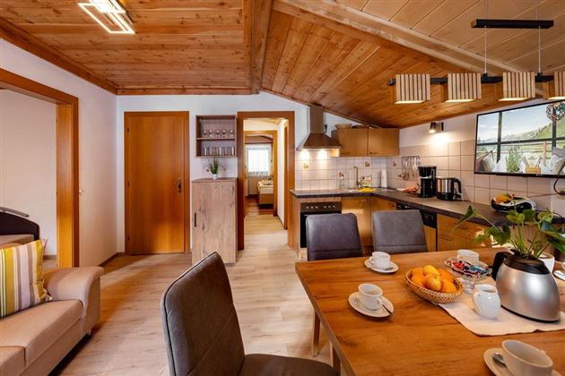 Eine gemütliche Wohnung mit Holzbalken und moderner Einrichtung. Der Tisch ist gedeckt mit Geschirr und frischen Früchten, während die Küche gut ausgestattet ist.